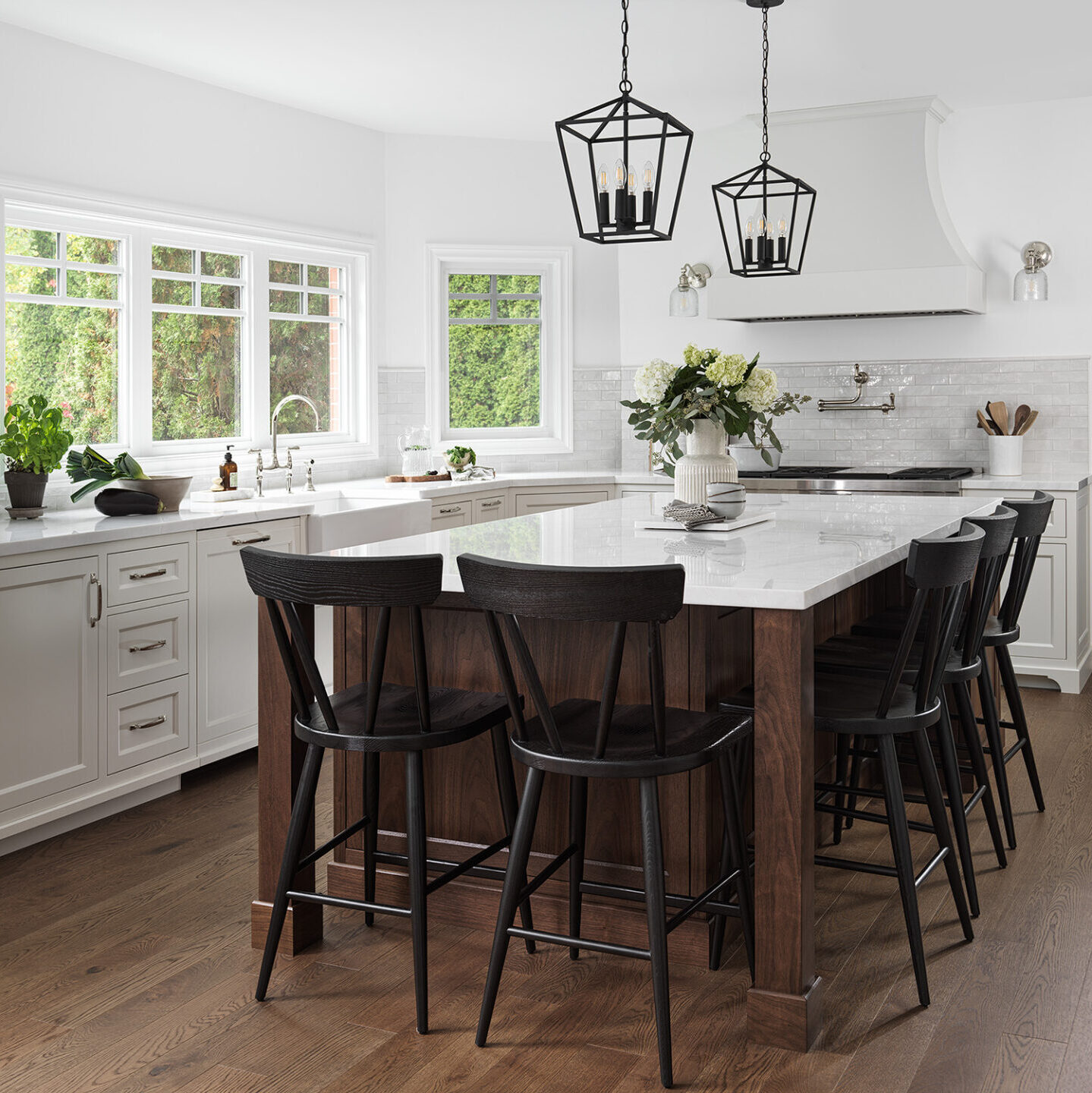 Bright white kitchen with rich wood-toned flooring. Kitchen island with white counter-top surrounded by black chairs. Longvalley Project by STILE Contracting + Design.
