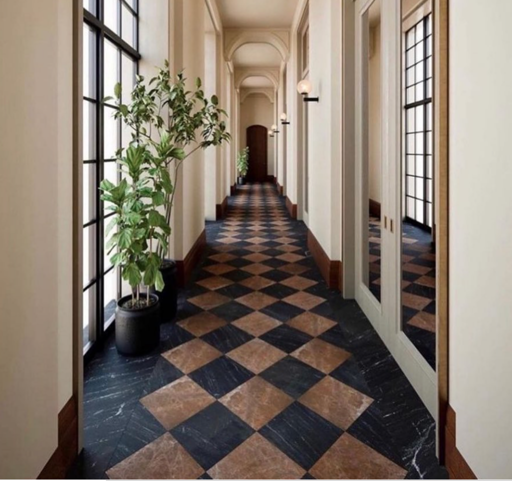 A long hallway in the Shinola Hotel with high arches, neutral tones and plants. Brown and black stone flooring.